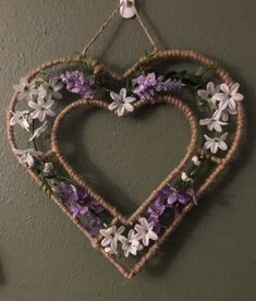 a heart shaped hanging on the wall with purple and white flowers in it's center