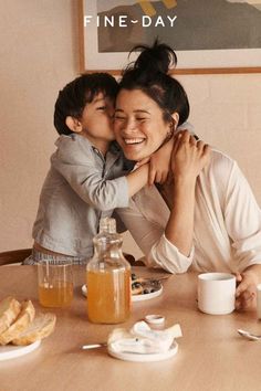 a woman and child sitting at a table with breakfast foods in front of them on the table