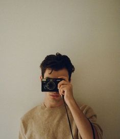 a young man holding up a camera to take a selfie in front of his face