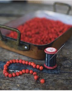 a spool of thread next to some red beads and a spool of thread