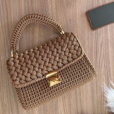 a brown woven purse sitting on top of a wooden table next to a cell phone