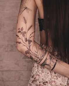 a woman's arm with flowers and dragonflies tattooed on her left arm, next to a brick wall