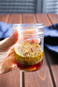 someone holding a jar filled with food on top of a wooden table