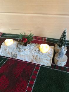 two lit candles sitting on top of a piece of wood next to some pine trees