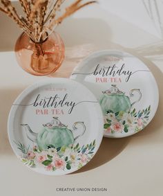 two paper plates decorated with teapots and flowers on the table next to a vase