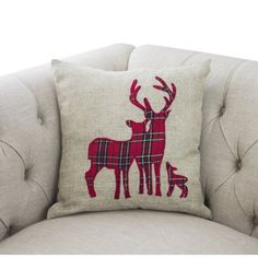 a red and white deer pillow sitting on top of a gray couch next to a small dog