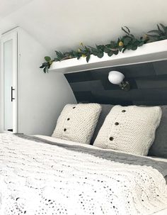 the bed is made and has two pillows on it, along with some greenery