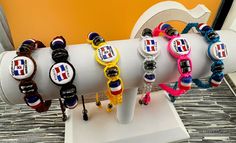 several bracelets on display in front of a yellow wall and white pedestal with black, blue, red, and white beads