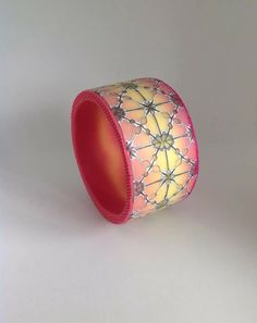 a pink and yellow lamp shade on a white surface with an orange light in the middle