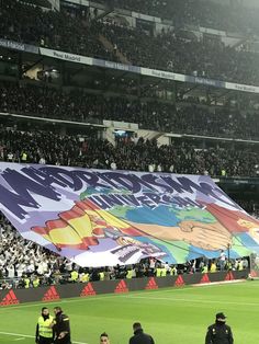 a large banner on the side of a soccer field with people standing around it in front of an audience