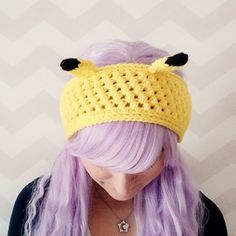 a woman with purple hair wearing a crocheted headband made to look like a bee