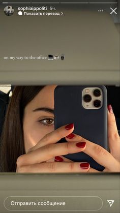 a woman looking at her cell phone in the mirror with red nail polish on her nails