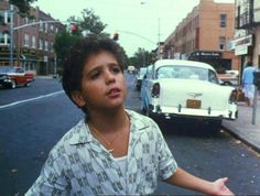 a young boy standing on the side of a road next to a white classic car