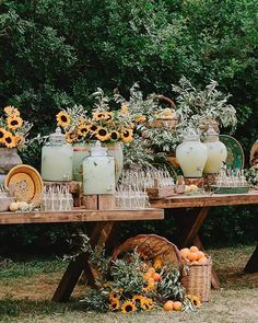 an outdoor table with sunflowers and vases on it, surrounded by greenery