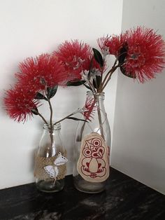 two vases with red flowers in them on a table next to a white wall