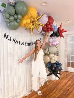 a woman standing in front of balloons and streamers on the wall with her arms up