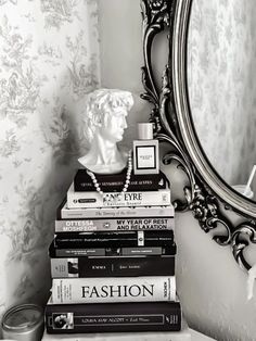 a stack of books sitting on top of a table next to a mirror and a busturine