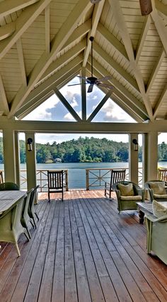 a wooden deck with chairs and tables on it next to the water in front of a pavilion