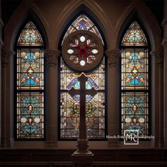 an ornate stained glass window with a cross in the center and other windows behind it