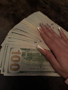 a woman's hand on top of stacks of twenty dollar bills with nails painted white