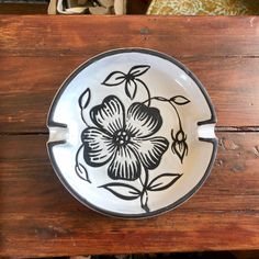 a black and white plate with flowers on it sitting on a wooden table next to a basket