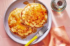 two pancakes sitting on top of a white plate next to a fork and glass of water