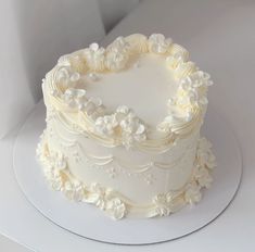 a heart shaped cake with white frosting and flowers on the top is sitting on a plate