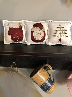 three embroidered christmas stockings are sitting on a shelf next to a coffee cup and mug