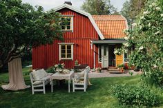 a red house with white chairs and tables in the front yard, surrounded by greenery