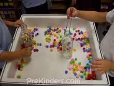 three children are playing with sprinkles in a play tray at the same time