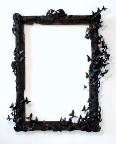 an old frame with butterflies on it is hanging on the wall in front of a white wall