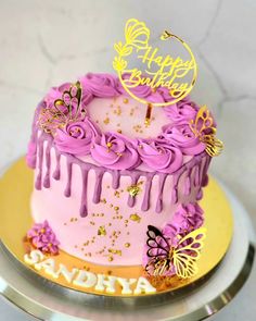 a pink birthday cake with purple icing and butterflies on it, sitting on a gold plate