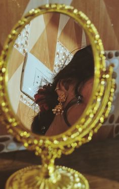 a woman is looking at her reflection in the mirror with gold beads on it's sides