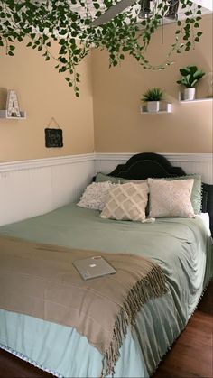 vines on ceiling, floating shelves with greenery, tan walls, sage green bed Sage Green And Tan Bedroom Aesthetic, Sage Green And Tan Aesthetic, Sage Minimalist Bedroom, Green And Tan Bedroom Ideas, Sage Green Bedding Bedroom, Sage Green Bedroom Ideas Aesthetic, Bedrooms With Vines, Vines In Bedroom Ideas, Green Vines Bedroom Decor