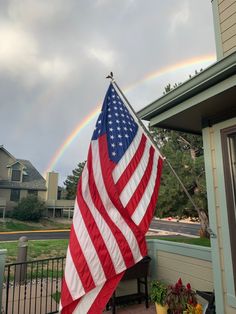 an american flag on a porch with a rainbow in the background and houses behind it