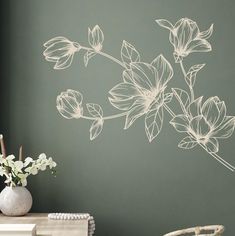 a white vase sitting on top of a table next to a wall with flowers painted on it