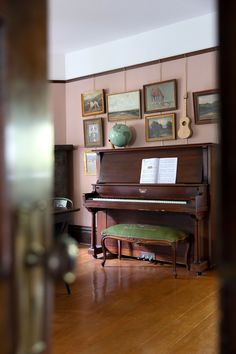 an old piano sits in the corner of a room with many pictures on the wall