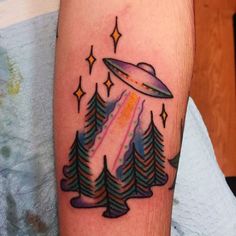 an alien tattoo on the arm with trees and flying saucer in the sky above it