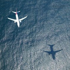 an airplane is flying low over the water and land, casting a shadow on the ground