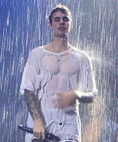 a young man standing in the rain with an open umbrella behind him and water pouring from his mouth