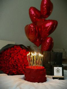 a red cake with candles on it sitting on a bed next to balloons and a box