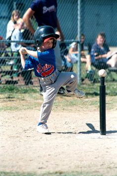 a young boy swinging a bat at a ball during a baseball game while people watch from the bleachers