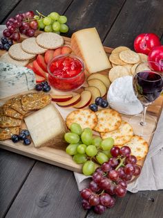 an assortment of cheeses, crackers and grapes on a wooden platter