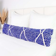 a blue and white pillow sitting on top of a bed next to a vase with flowers