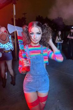 a woman in overalls and colorful makeup is holding a large ax on her shoulder