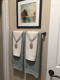 two towels hanging on a towel rack in a bathroom next to a framed painting and door