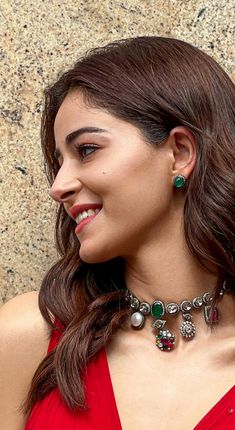 a woman in a red dress is smiling and wearing a necklace with charms on it