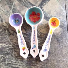 three spoons with flowers painted on them are sitting on a marble counter top,