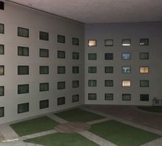 an empty room with windows and grass in the floor, next to a wall that has squares on it