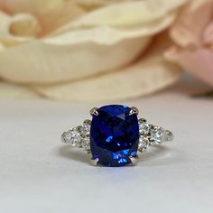 a ring with a blue stone surrounded by three diamonds and a rose in the background